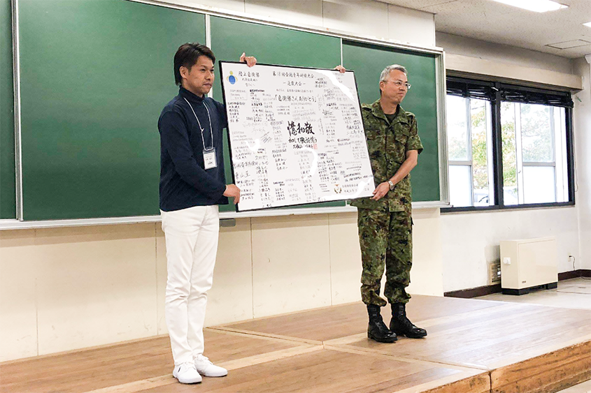 全国防衛協会連合会青年部 第18回全国青年研修大会「近畿大会」部隊研修において、日頃の感謝の気持ちを込めた寄せ書きを、基地司令にお渡しする。